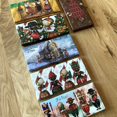 Várias caixas de chocolates natalícios decoradas com personagens tradicionais sobre madeira clara