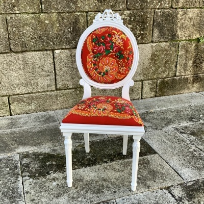 Cadeira branca com estofado vermelho floral em parede e chão de pedra
