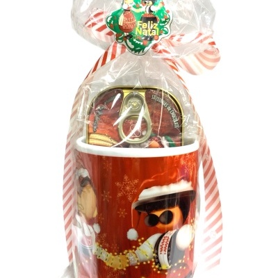 Caneca vermelha com boneco de Natal embalada em saco plástico com fita e etiqueta de Feliz Natal