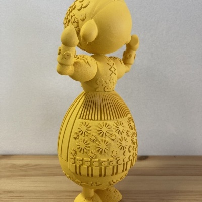 Figura decorativa amarela com vestido e chapéu detalhados em padrão floral e geométrico