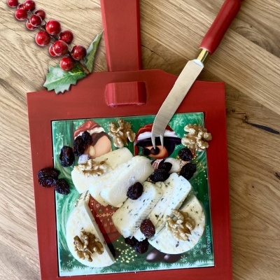 Tábua vermelha com queijo, nozes, faca e decoração de Natal em superfície de madeira.