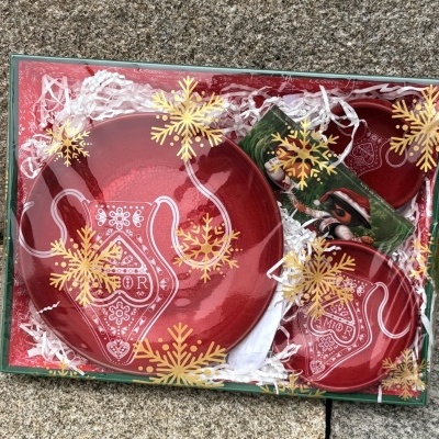 Conjunto de loiça vermelha com motivos tradicionais e a palavra AMOR em embalagem decorada com flocos de neve.