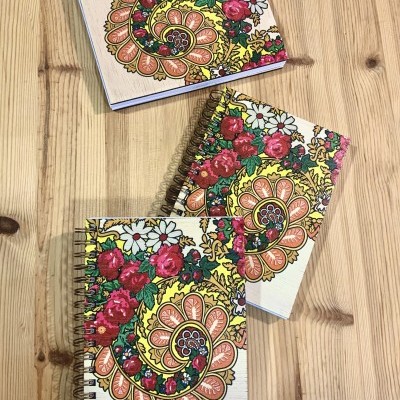 Três cadernos com capa floral e espiral sobre mesa de madeira clara