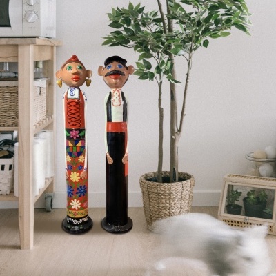 Esculturas de madeira coloridas de figuras humanas junto a planta e móvel de madeira