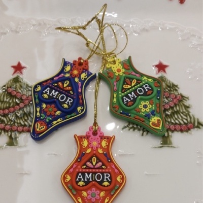 Três ornamentos coloridos com a palavra AMOR sobre um prato decorativo com pinheiros e estrelas