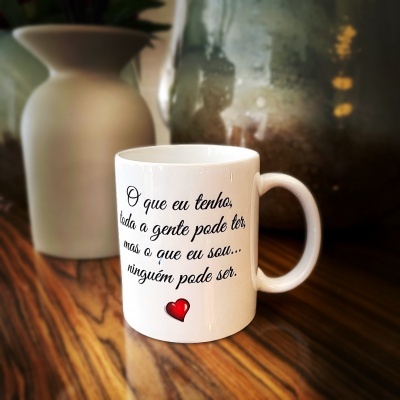 Caneca branca com texto em português e um coração vermelho, sobre mesa de madeira