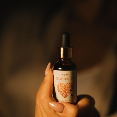 Frasco de vidro castanho com conta-gotas e etiqueta 'NEW SILHOUETTE' na mão de mulher