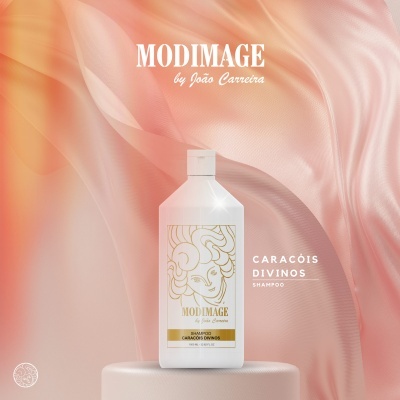 Frasco branco de shampoo MODIMAGE Caracóis Divinos com design dourado e branco sobre superfície cilíndrica cor creme e fundo rosa e laranja