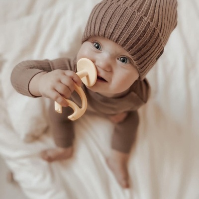Bebé com gorro castanho e anel de dentição amarelo claro em fundo branco