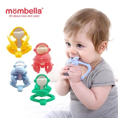 Bebé a usar mordedor azul com outros mordedores coloridos e logo mombella