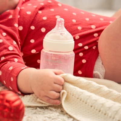 Bebé de body vermelho com bolinhas a segurar mamadeira transparente