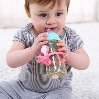 Bebé sentado com biberão transparente com pega em forma de estrela do mar cor-de-rosa