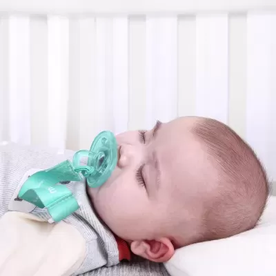 Bebé deitado com chupeta verde presa à roupa por fita verde