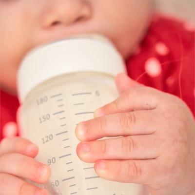 Bebé a segurar um frasco de leite transparente com marcações ml até 180