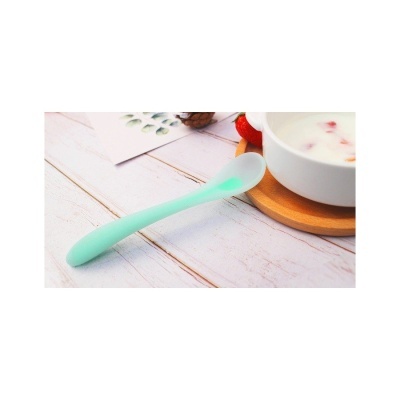 Colher de silicone verde água junto a tigela branca sobre superfície de madeira