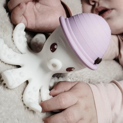 Brinquedo de polvo branco com chapéu lilás junto às mãos de um bebé