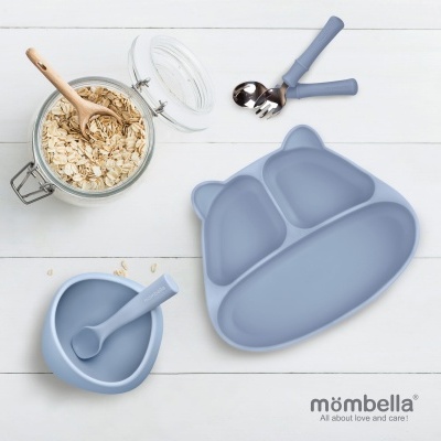 Conjunto de alimentação infantil em silicone azul com prato dividido, colher, taça e talheres sobre superfície branca