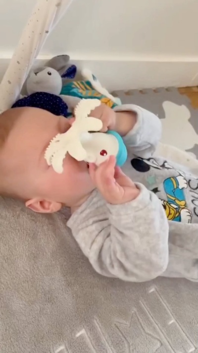 Bebé com brinquedo de silicone branco a morder no tapete cinzento