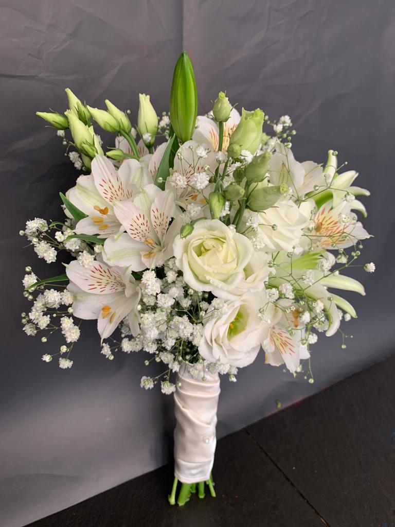 Buquê de flores brancas com rosas e lírios envolto em fita branca em fundo cinzento