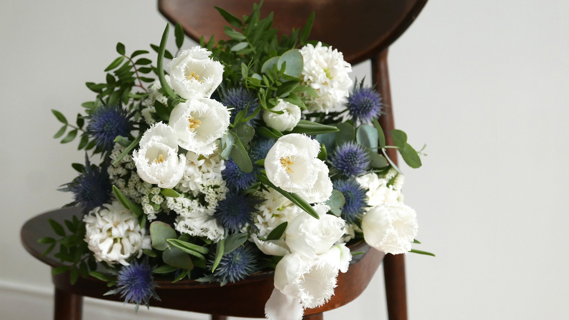 Bouquet de flores branco e azul sobre banco de madeira escura