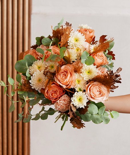 Ramo de flores com rosas pêssego, crisântemos brancos e folhas verdes em fundo claro