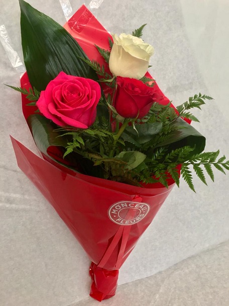 Ramo de três rosas coloridas e folhagens num embrulho vermelho com etiqueta MONCEAL FLORES