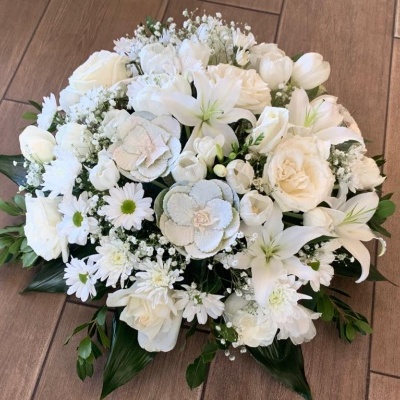 Arranjo floral branco com folhas verdes sobre chão de madeira clara