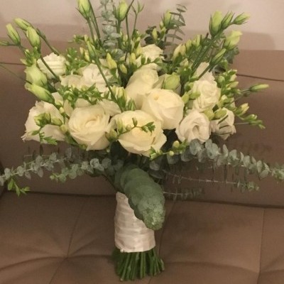 Buquê de flores brancas com folhagem verde numa fita branca sobre sofá castanho