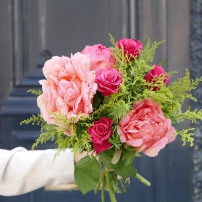 Buquê de flores rosa e verde segurado por mão em frente a porta preta