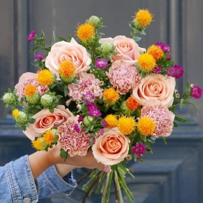 Buquê colorido de rosas e flores pequenas segurado à mão com porta azul ao fundo
