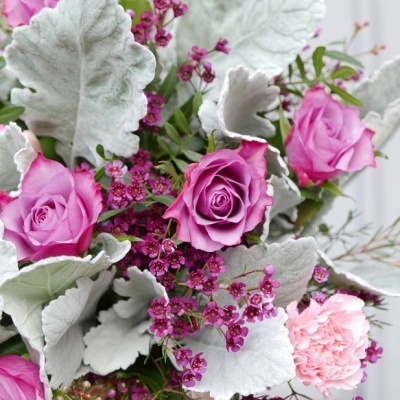 Bouquet de flores com rosas cor de rosa, cravos, folhas verde-acinzentadas e pequenas flores roxas