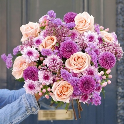Ramo de flores cor de salmão e lilás segurado por mão com camisa azul