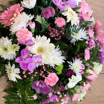 Arranjo floral multicolorido com flores brancas, rosas e lilás sobre piso de madeira.