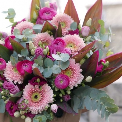 Ramo de flores cor-de-rosa e champanhe com folhas verdes e vermelhas num vaso castanho claro