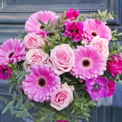 Buquê de flores rosas e fúcsia com folhagem verde em frente a porta cinzenta