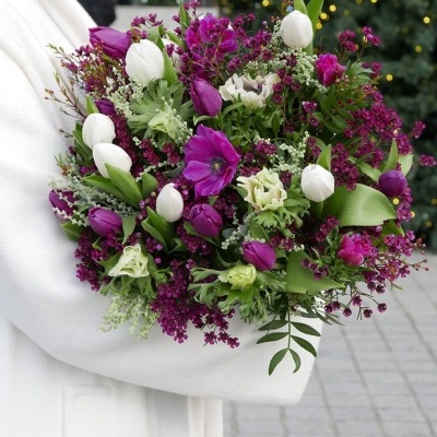 Bouquet de flores com tulipas brancas e roxas e folhagem, segurado ao ar livre.