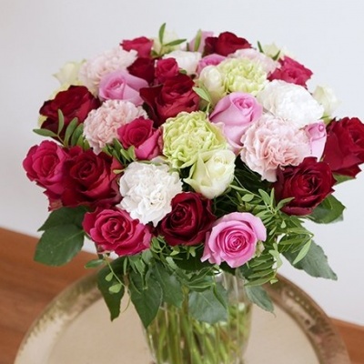 Bouquet colorido de rosas e flores em vaso transparente numa mesa metálica dourada