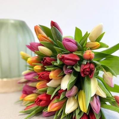 Ramo colorido de tulipas sobre mesa clara com vaso verde ao fundo