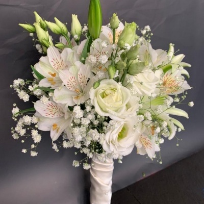 Buquê de flores brancas com rosas e lírios envolto em fita branca em fundo cinzento