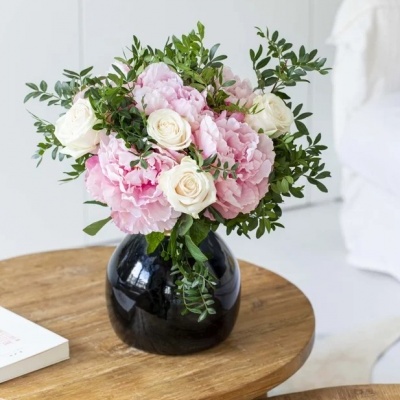 Arranjo floral com flores brancas e cor-de-rosa num vaso preto sobre mesa de madeira