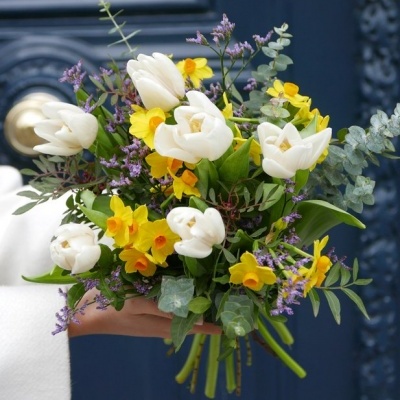 Buquê colorido de flores variadas com talos verdes na mão contra fundo azul escuro