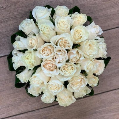 Buquê de rosas brancas redondo com folhas verdes sobre fundo de madeira clara