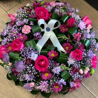 Coroa de flores colorida com laço branco sobre chão de tijoleira