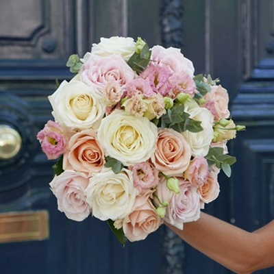 Buquê de rosas creme, branco e salmão com flores rosas pequenas e folhas verdes em frente a porta azul.