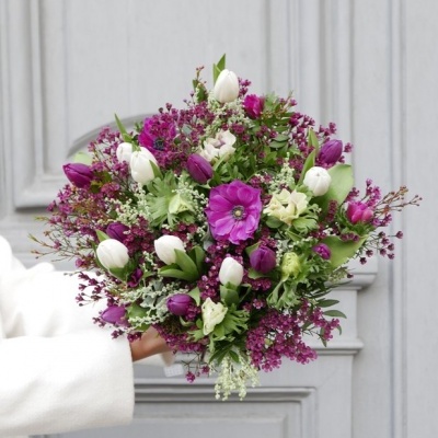 Ramo de flores roxas e brancas com folhagem diversificada, diante de uma porta cinzenta.