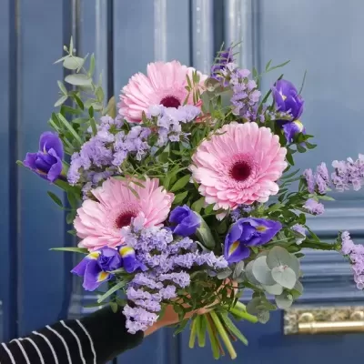 Buquê de flores cor-de-rosa, roxas e verdes segurado por pessoa em frente a porta azul