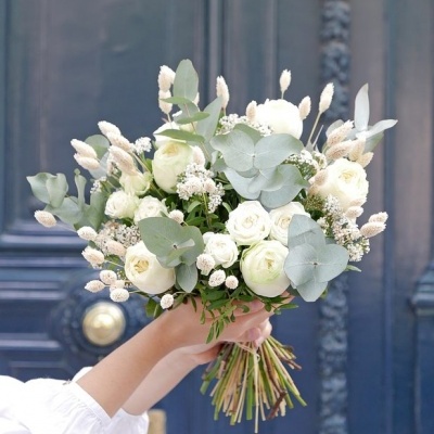 Bouquet de flores brancas e verdes segurado em frente a uma porta azul