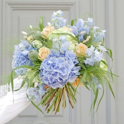 Buquê de flores azuis, creme e verde com porta cinza ao fundo