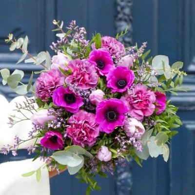 Buquê de flores rosa e roxas com folhagem verde em fundo de porta azul escuro.