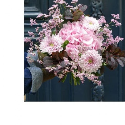 Ramo de flores rosa segurado por mão com manga azul junto a porta azul escura